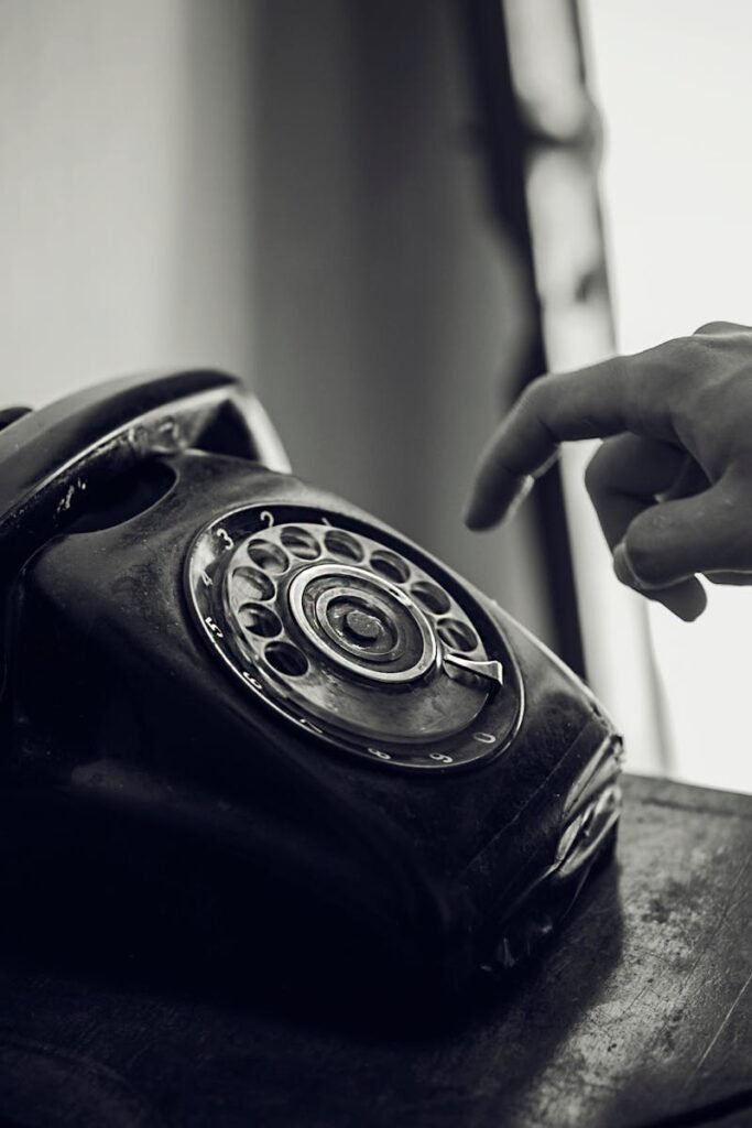 pexels photo 1006122 1006122 A monochrome photo of a hand reaching towards a vintage black rotary telephone in an indoor setting.